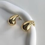 Gold teardrop-shaped stud earrings with posts resting on a white plate surface.