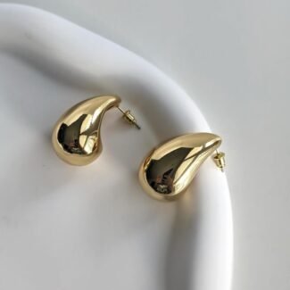 Gold teardrop-shaped stud earrings with posts resting on a white plate surface.