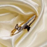 Gold bracelet with a row of small diamonds and two butterfly charms, one white and one black, resting on cream satin.