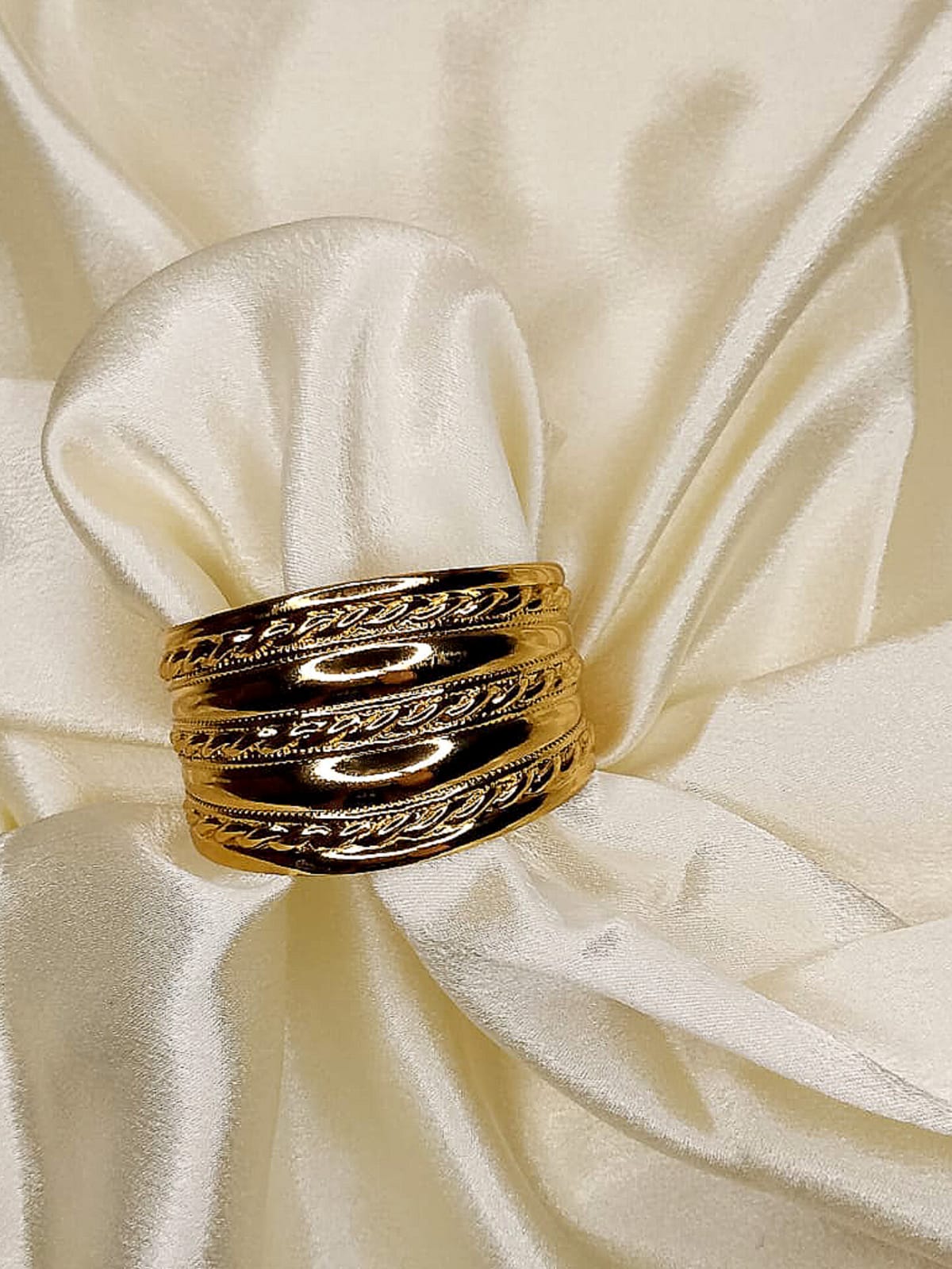 Gold stacked bangles with braided edges on ivory satin fabric.