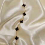 Gold chain necklace with black four-leaf clover charms laid on cream satin fabric.