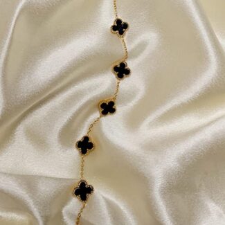 Gold chain necklace with black four-leaf clover charms laid on cream satin fabric.