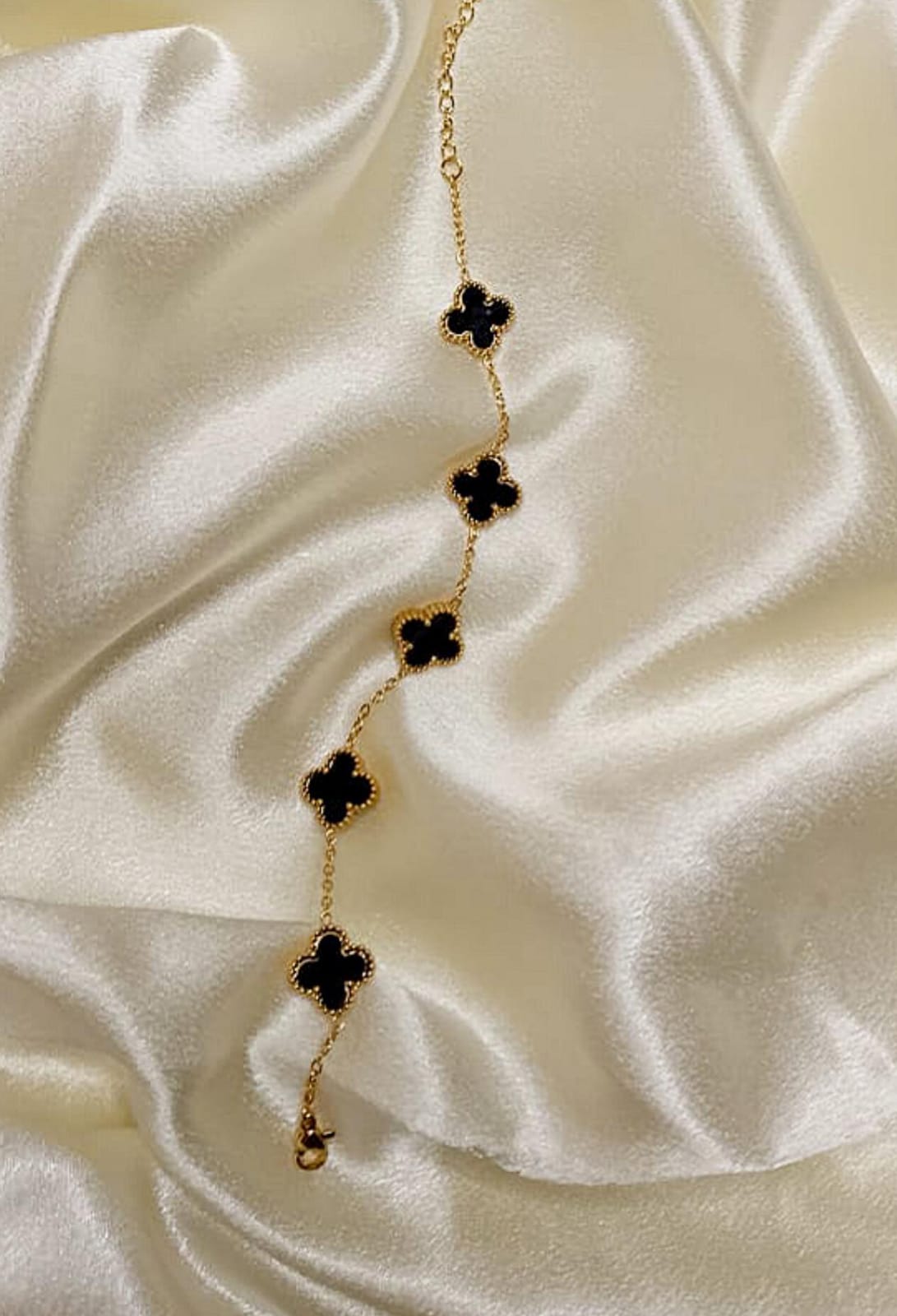 Gold chain necklace with black four-leaf clover charms laid on cream satin fabric.