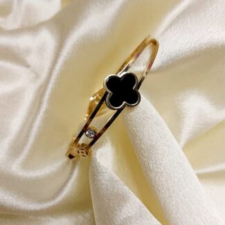 Gold bracelet with a black four-leaf-clover charm resting on ivory satin fabric, with a small diamond accent nearby.