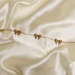 Delicate gold chain bracelet with small bow charms on ivory satin backdrop.