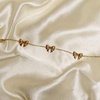 Delicate gold chain bracelet with small bow charms on ivory satin backdrop.