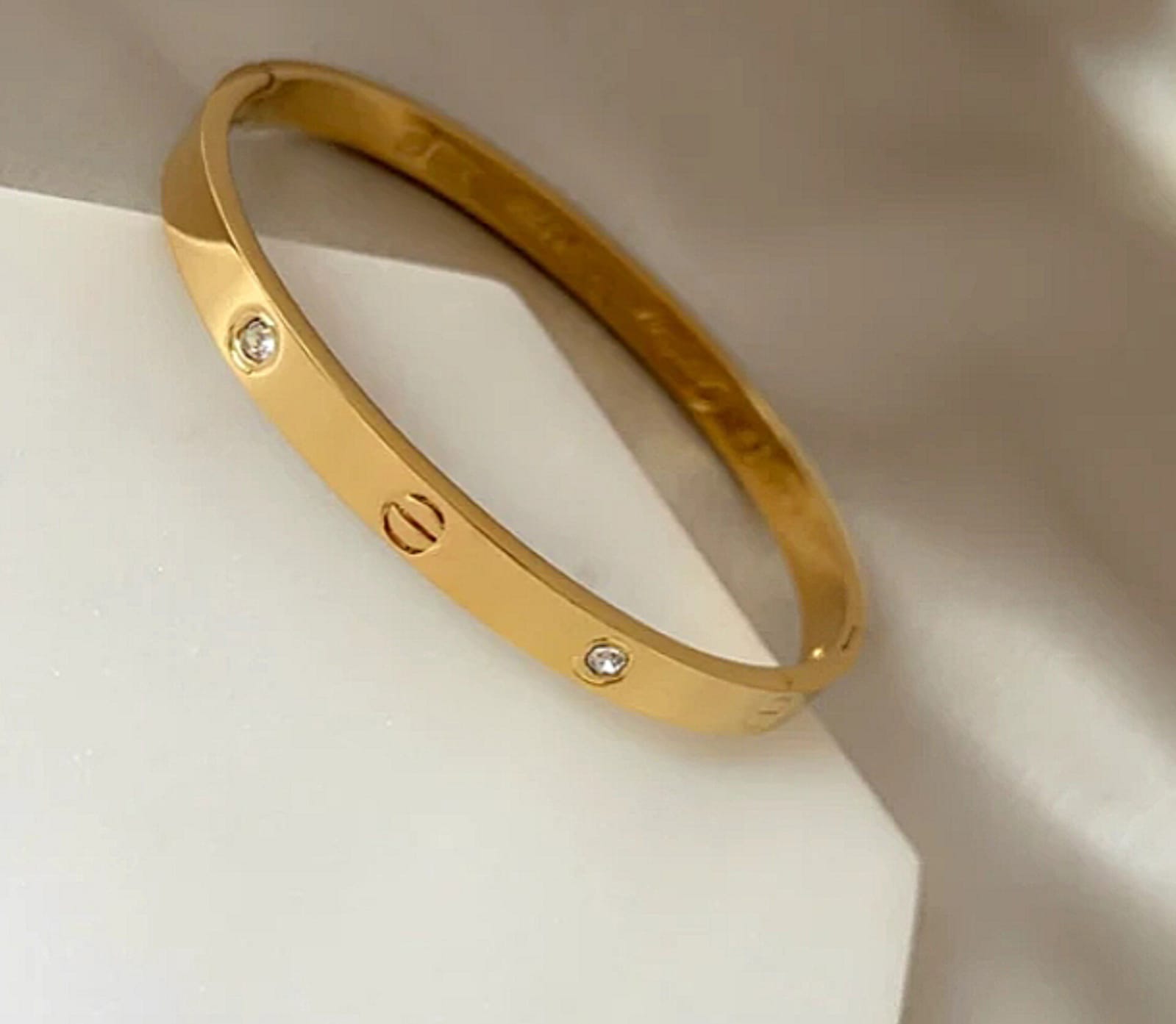 Gold bracelet with small diamond accents resting on a white surface, showing screw-like details along the band.