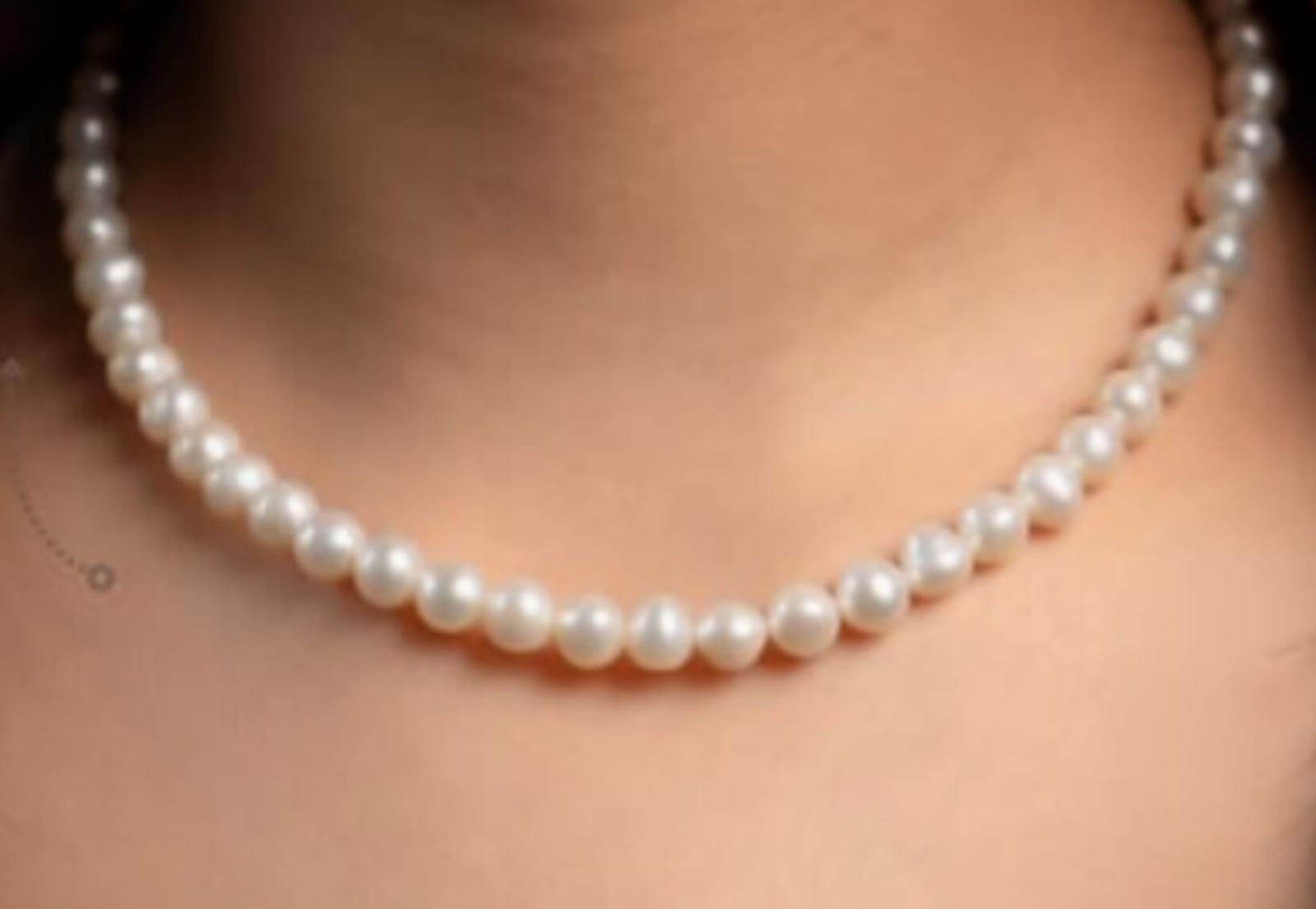 Close-up of a single-strand pearl necklace draped along the neck and collarbone.