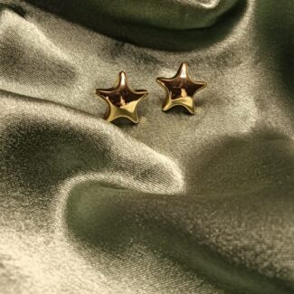 Two gold star-shaped earrings resting on shimmering olive satin fabric.