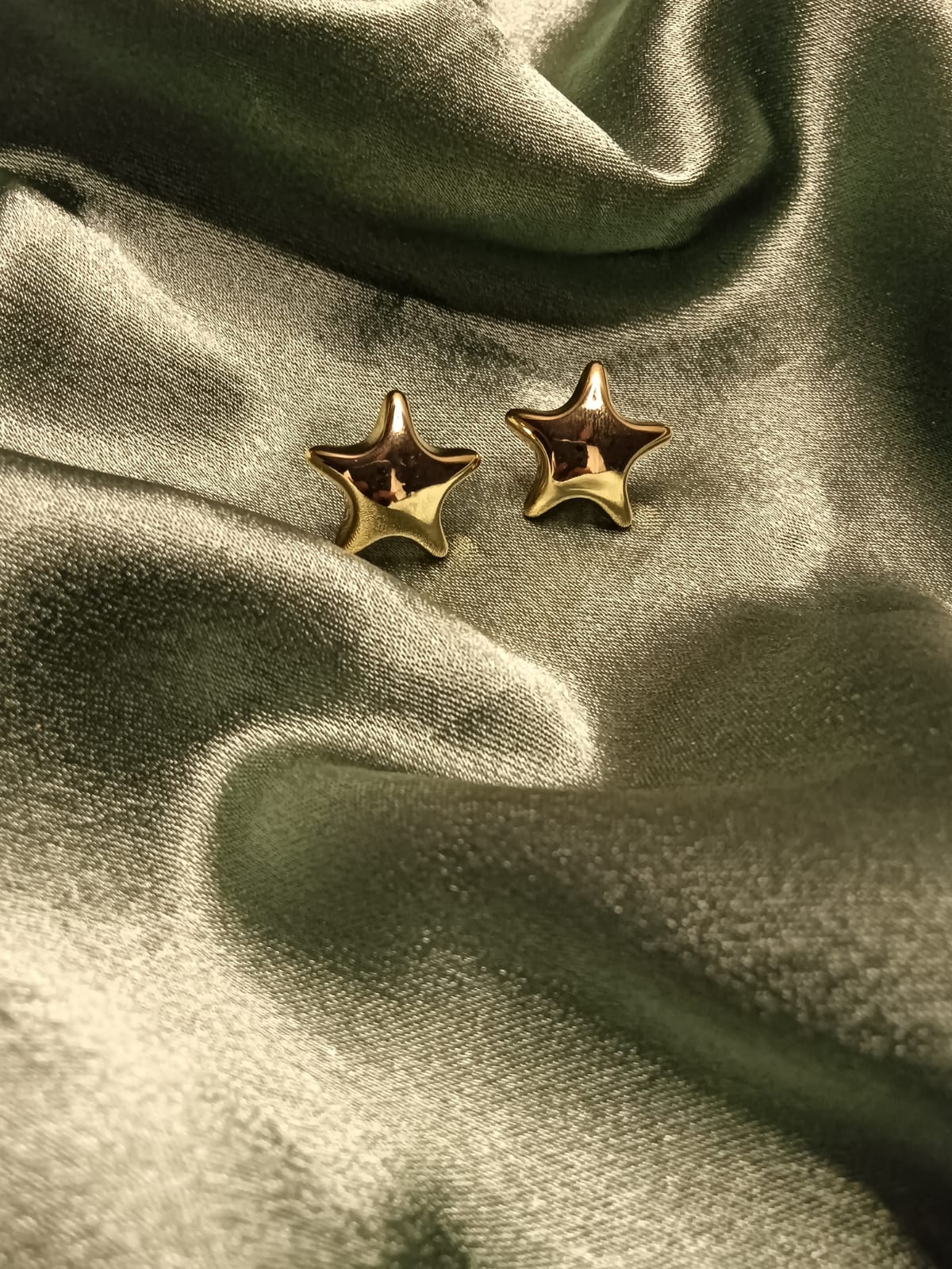 Two gold star-shaped earrings resting on shimmering olive satin fabric.