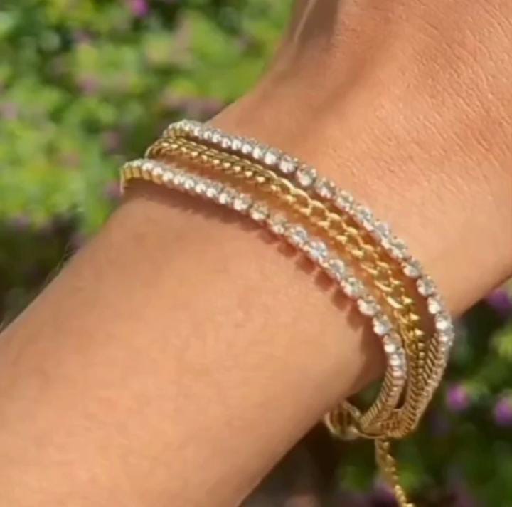 Wrist wearing multiple stacked gold and diamond tennis bracelets with clear stones gleaming in sunlight.