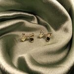 Gold bow-shaped stud earrings resting on emerald green satin fabric