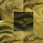 Gold bow-shaped stud earrings arranged on olive-green satin fabric. Decorative jewelry display.