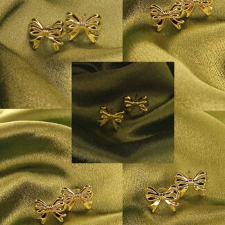 Gold bow-shaped stud earrings arranged on olive-green satin fabric. Decorative jewelry display.