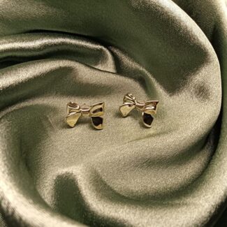 Gold bow-shaped stud earrings resting on emerald green satin fabric