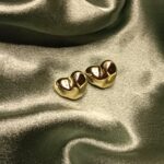 Pair of shiny gold dental crowns resting on dark satin fabric.