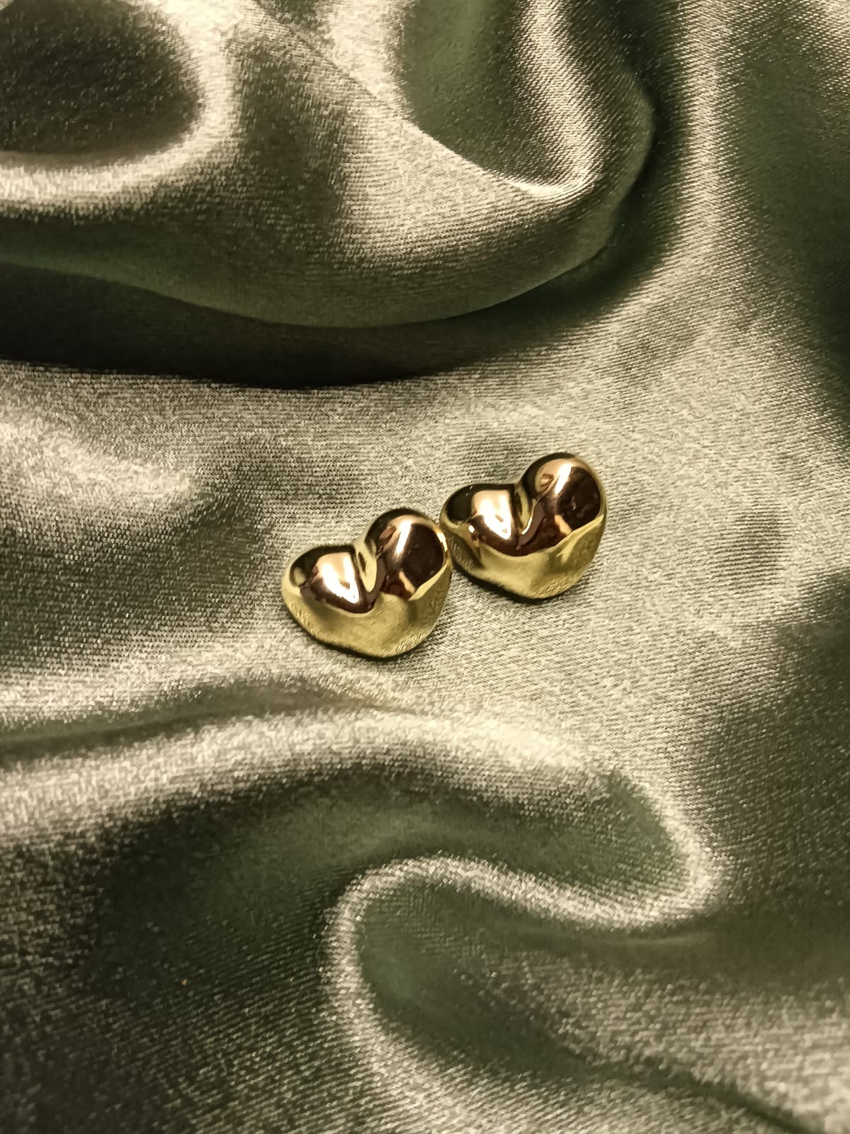 Pair of shiny gold dental crowns resting on dark satin fabric.