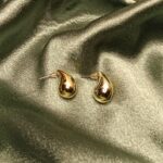 Pair of gold teardrop-shaped earrings resting on green satin fabric