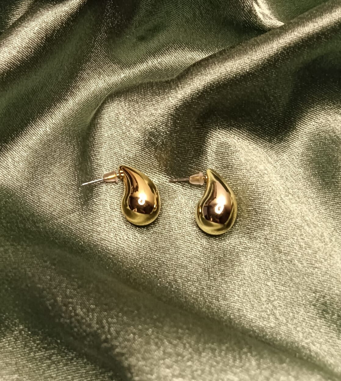 Pair of gold teardrop-shaped earrings resting on green satin fabric