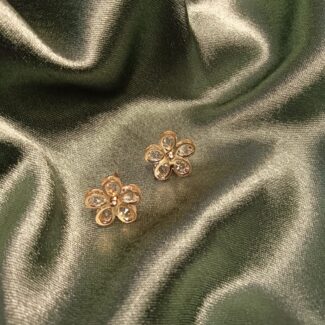 Gold-tone flower-shaped earrings with clear gemstones, placed on dark green satin fabric.
