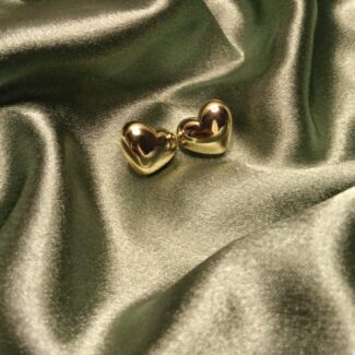 Two small gold heart earrings resting on green satin fabric, gleaming in the light.