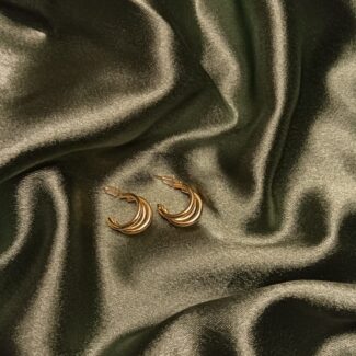 Gold multi-band crescent hoop earrings resting on dark satin fabric.