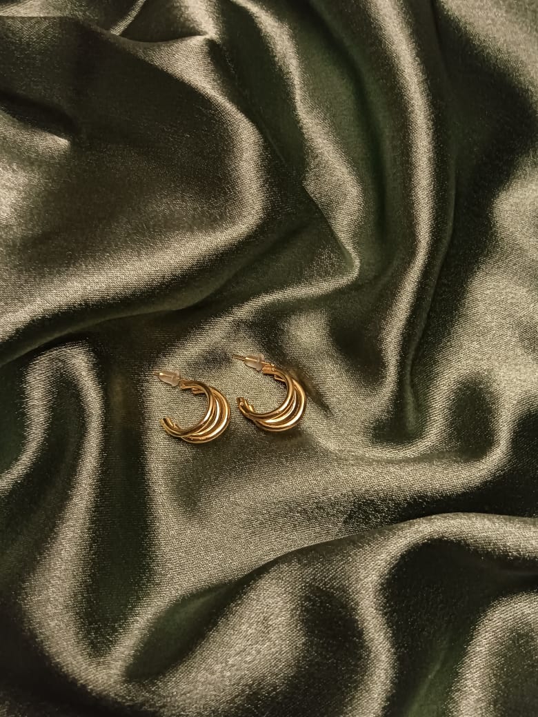 Gold multi-band crescent hoop earrings resting on dark satin fabric.