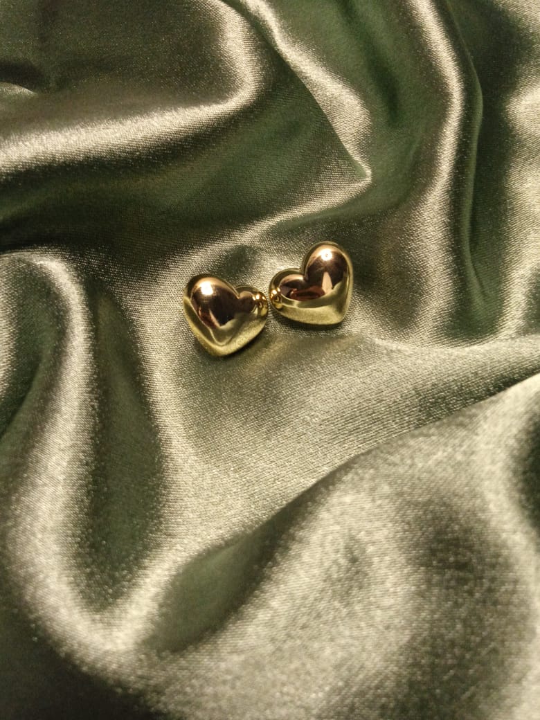 Two small gold heart earrings resting on green satin fabric, gleaming in the light.