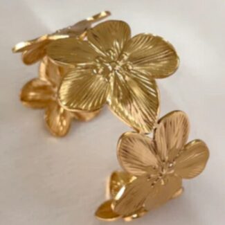 Gold-tone flower-shaped jewelry pieces with five textured petals resting on a pale surface