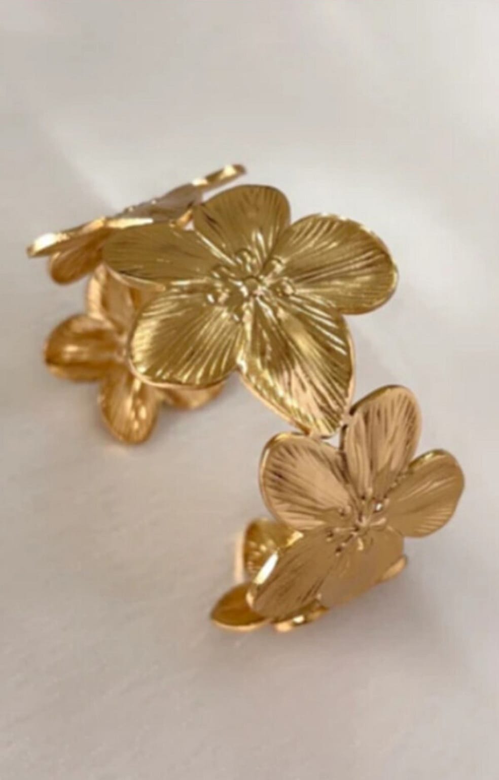 Gold-tone flower-shaped jewelry pieces with five textured petals resting on a pale surface