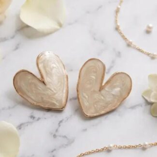Two heart-shaped earrings with iridescent cream interiors and rose-gold edges, resting on a marble surface.