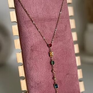 Copper-toned necklace with a row of small colored gems, displayed on a pink velvet stand with a wooden frame.