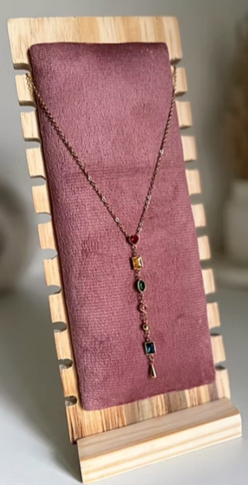 Copper-toned necklace with a row of small colored gems, displayed on a pink velvet stand with a wooden frame.