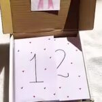 Card with the number 12 and small hearts inside an open cardboard box (gift box). зб
