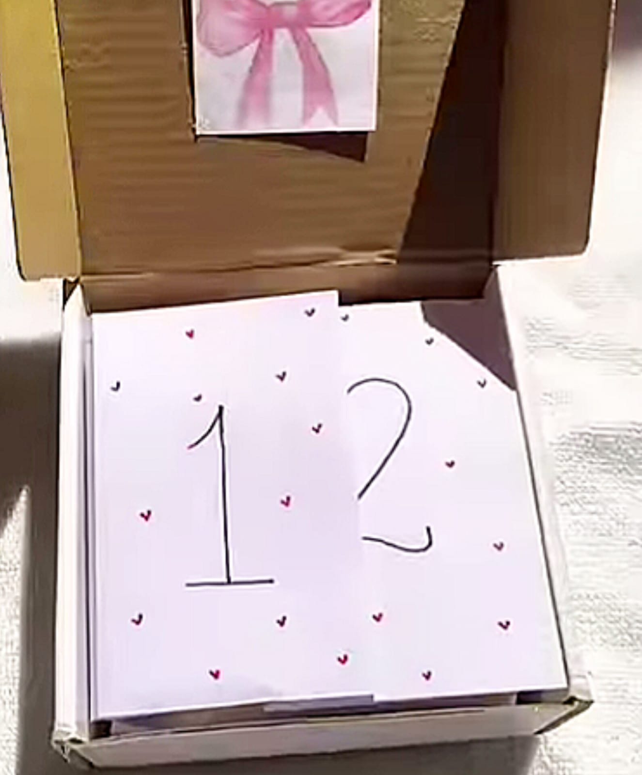 Card with the number 12 and small hearts inside an open cardboard box (gift box). зб