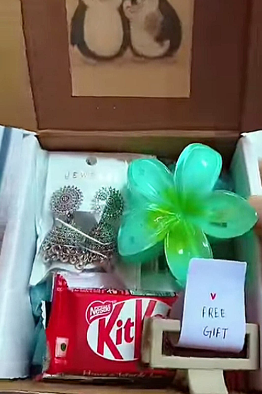 Gift box with a red KitKat bar, a bright green plastic flower pinwheel, and a small note reading 'V FREE GIFT' inside.