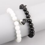Two stretch bracelets—one white, one black—with a small silver heart charm, shown on a neutral display arm.