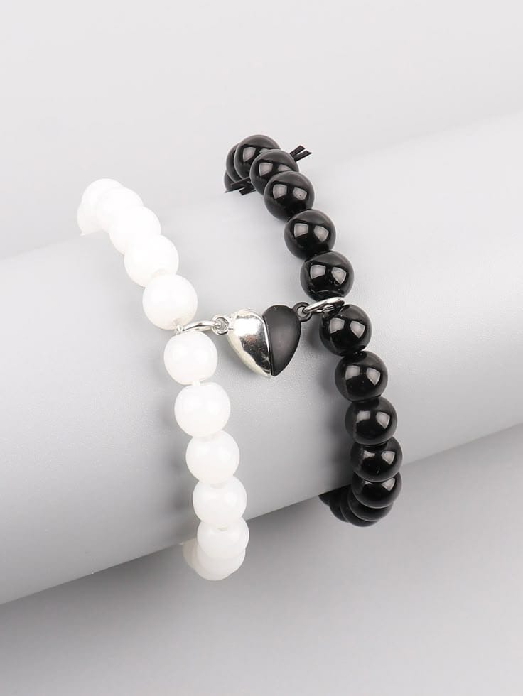 Two stretch bracelets—one white, one black—with a small silver heart charm, shown on a neutral display arm.
