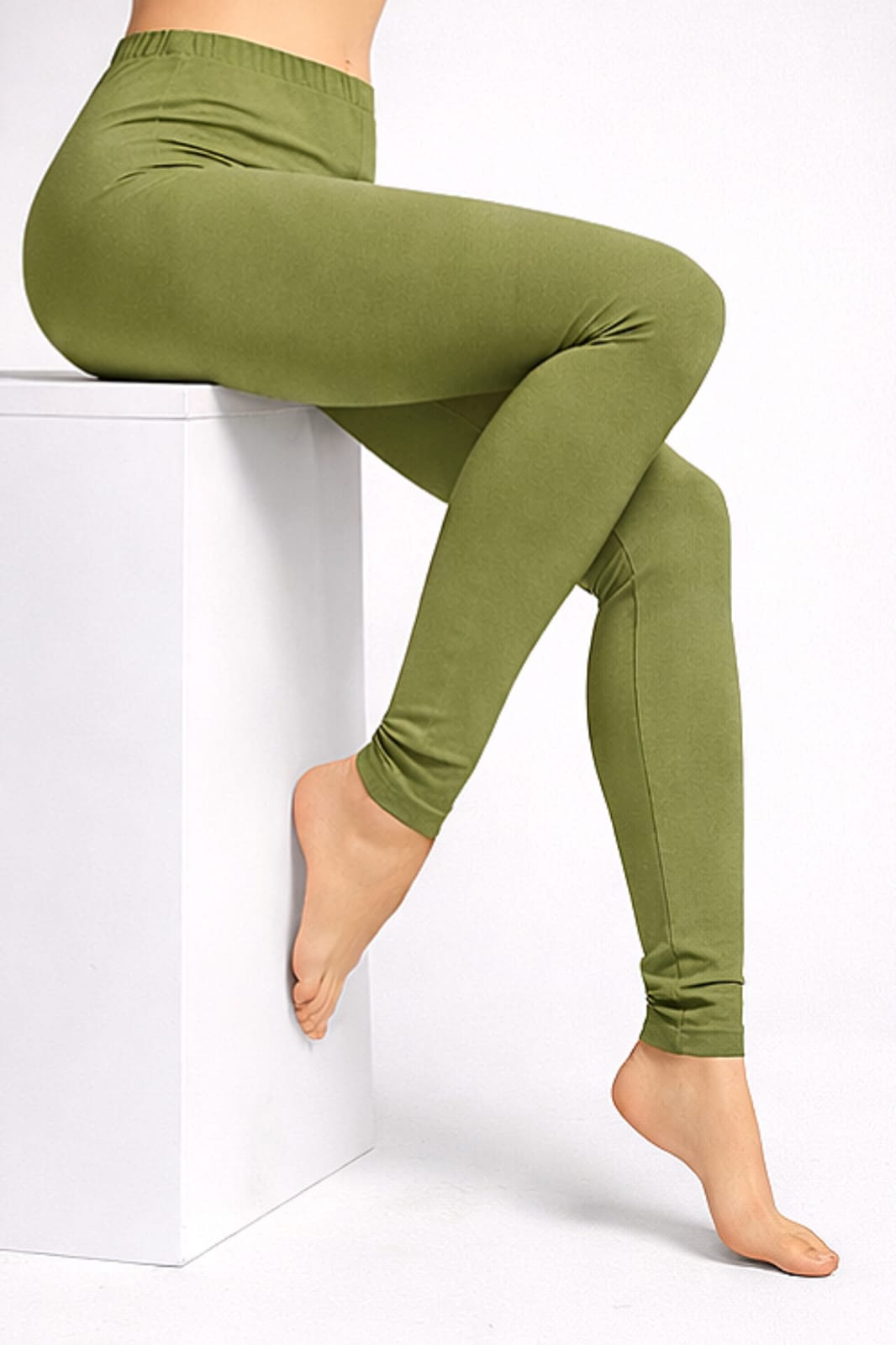 Person seated on a white block wearing olive-green leggings, feet bare.