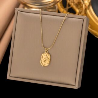 Gold pendant necklace with a rose engraving on a thin chain shown on a beige jewelry box in a display setting.