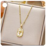 Gold pendant necklace with a floral design resting in a beige jewelry box on a chain above it.