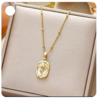 Gold pendant necklace with a floral design resting in a beige jewelry box on a chain above it.