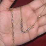 Delicate gold necklace with a vine-like chain and pink-purple gemstones, resting in a hand.