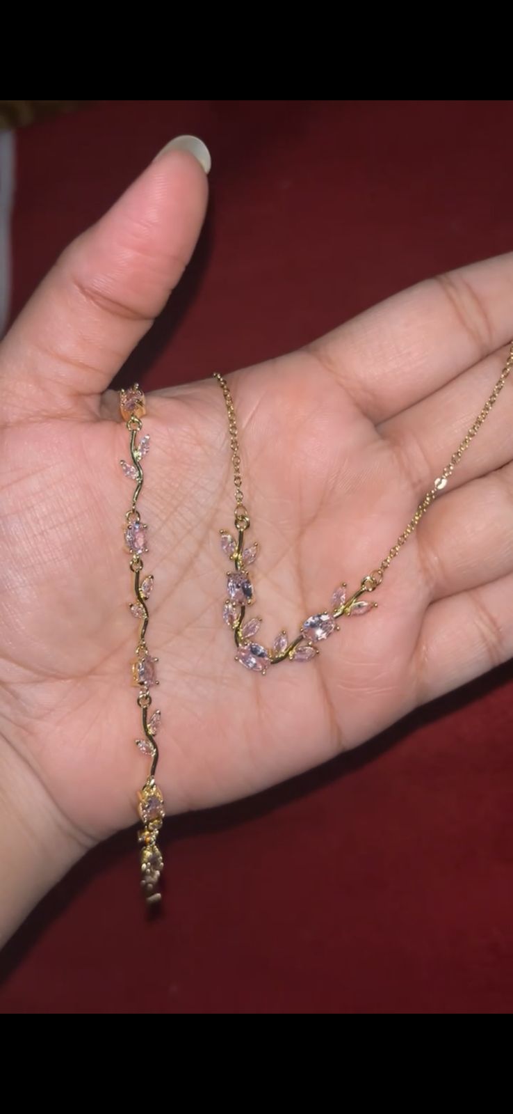 Delicate gold necklace with a vine-like chain and pink-purple gemstones, resting in a hand.