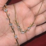 Gold necklace with vine-like branches and clear gemstone accents held in a palm magnified view of the jewelry design
