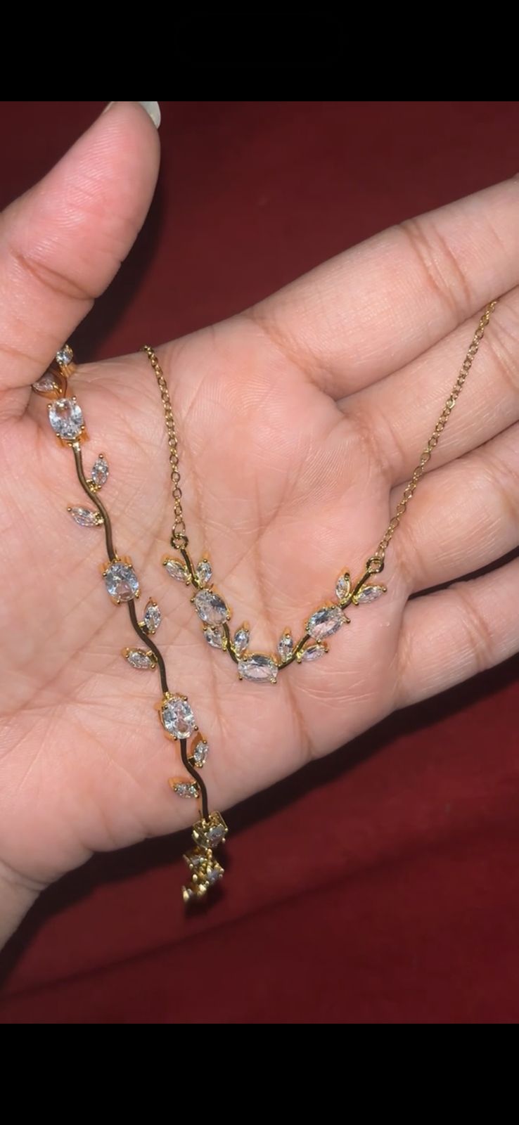 Gold necklace with vine-like branches and clear gemstone accents held in a palm magnified view of the jewelry design
