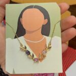 Illustrated jewelry card: a faceless figure wearing a gold necklace with pink, purple, and clear stones.