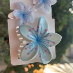 Three blue butterfly/flower hair clips attached to a white display card.