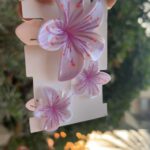 Three lavender orchid-shaped hair clips on a white display card, held by a hand outdoors.
