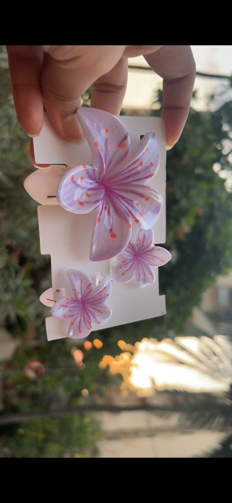 Three lavender orchid-shaped hair clips on a white display card, held by a hand outdoors.